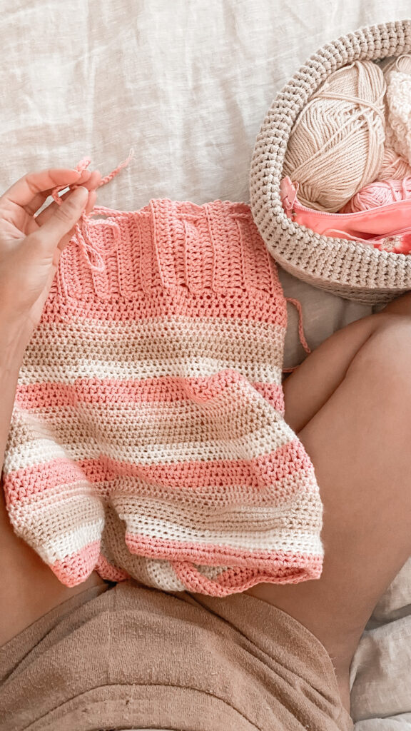 Flat lay of striped, made to measure crochet shorts in light pink, white, and beige.